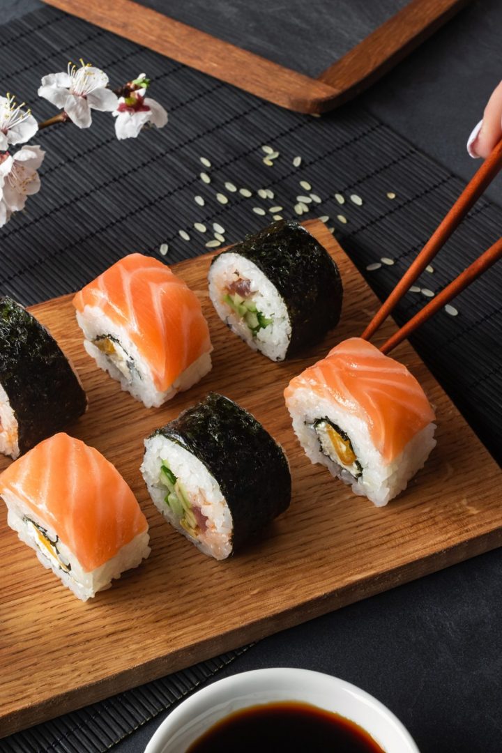 set-sushi-maki-rolls-hand-with-chopsticks-branch-white-flowers-stone-table-top-view-scaled.jpg